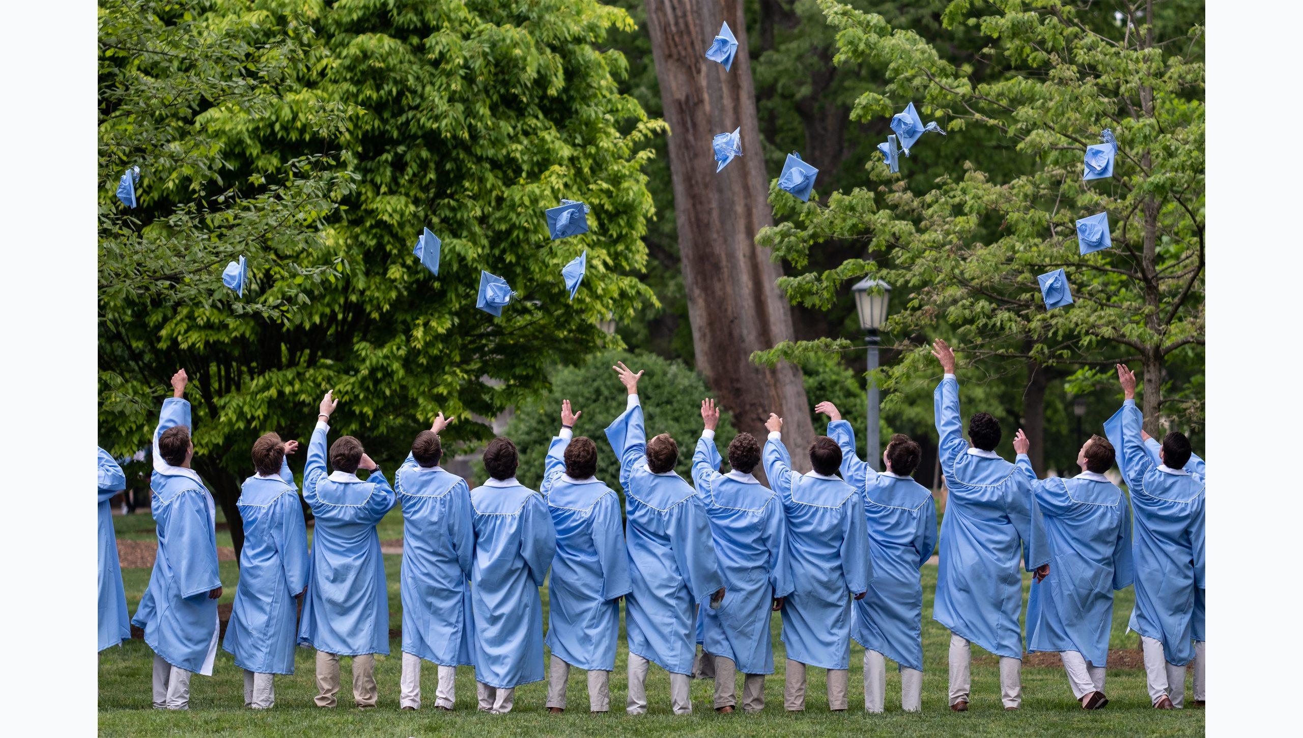 A group of students in regalia throwing caps up in their air for their group graduation photo.